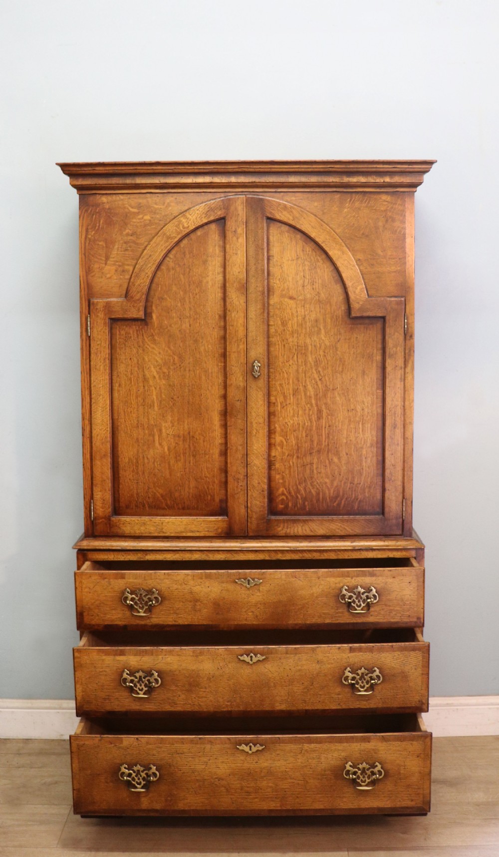 A Georgian style warm brown oak bureau cabinet featuring two upper arched doors opening to a fitted interior of pigeonholes and small drawers above three long drawers with brass handles. View IV