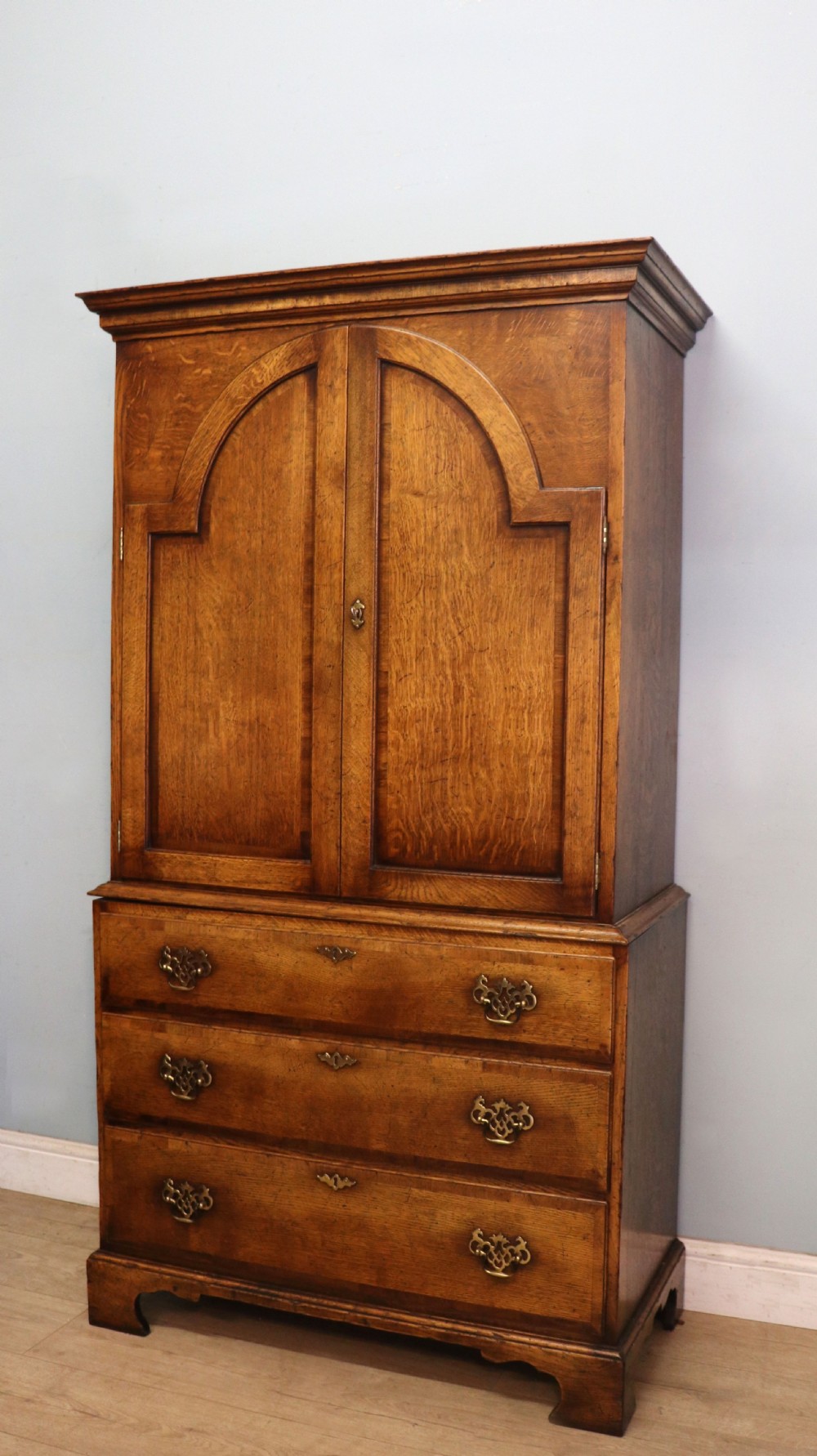 A Georgian style warm brown oak bureau cabinet featuring two upper arched doors opening to a fitted interior of pigeonholes and small drawers above three long drawers with brass handles. View VI