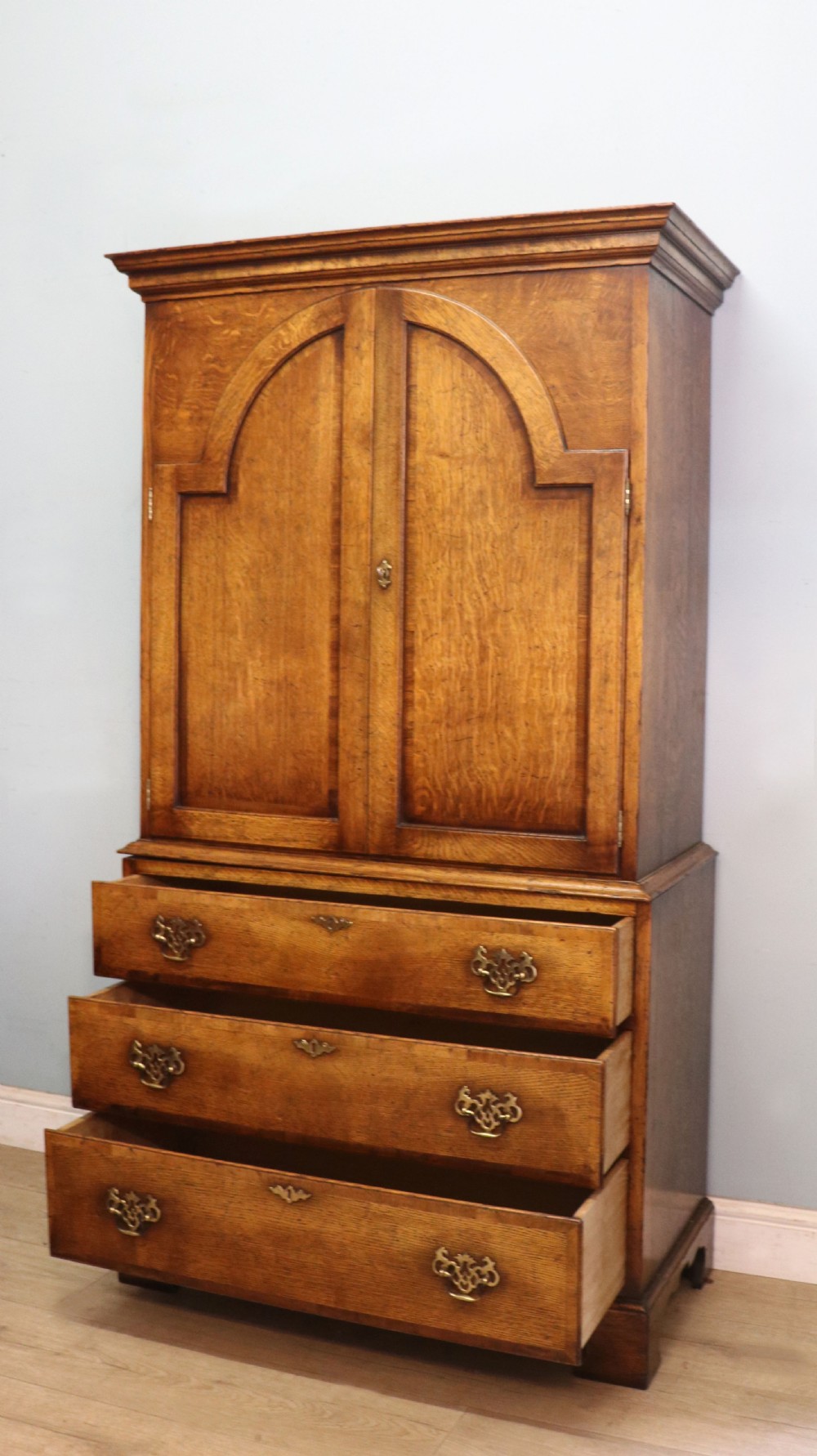 A Georgian style warm brown oak bureau cabinet featuring two upper arched doors opening to a fitted interior of pigeonholes and small drawers above three long drawers with brass handles. View VII