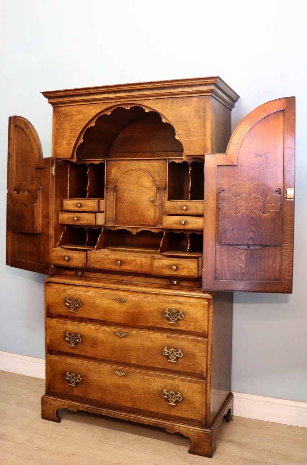 A Georgian style warm brown oak bureau cabinet featuring two upper arched doors opening to a fitted interior of pigeonholes and small drawers above three long drawers with brass handles. View VIII