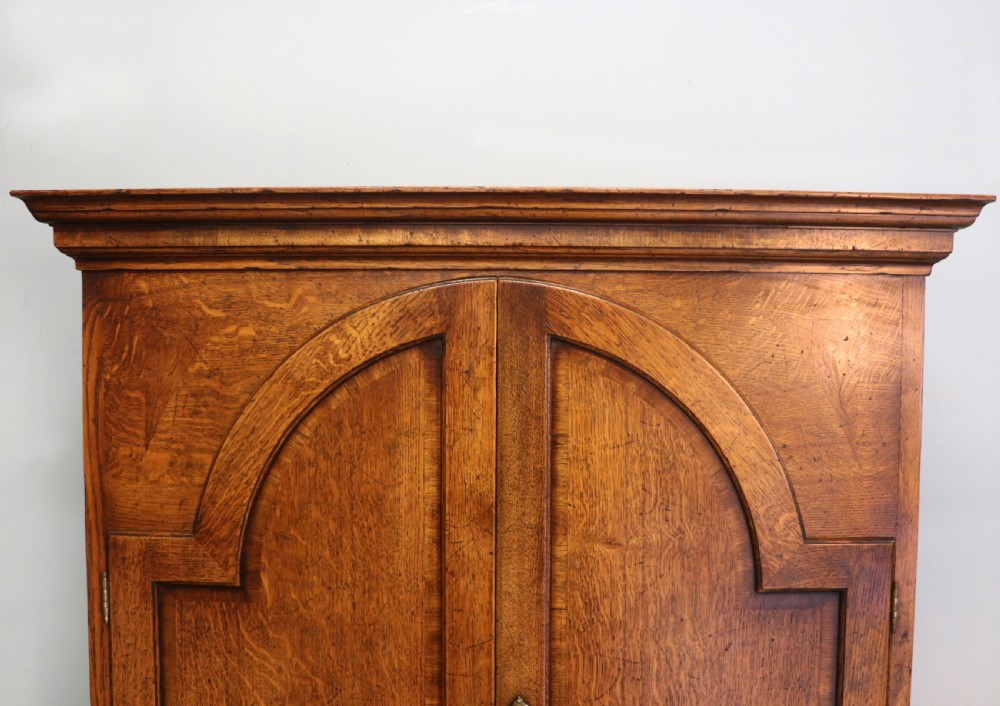 A Georgian style warm brown oak bureau cabinet featuring two upper arched doors opening to a fitted interior of pigeonholes and small drawers above three long drawers with brass handles. View X