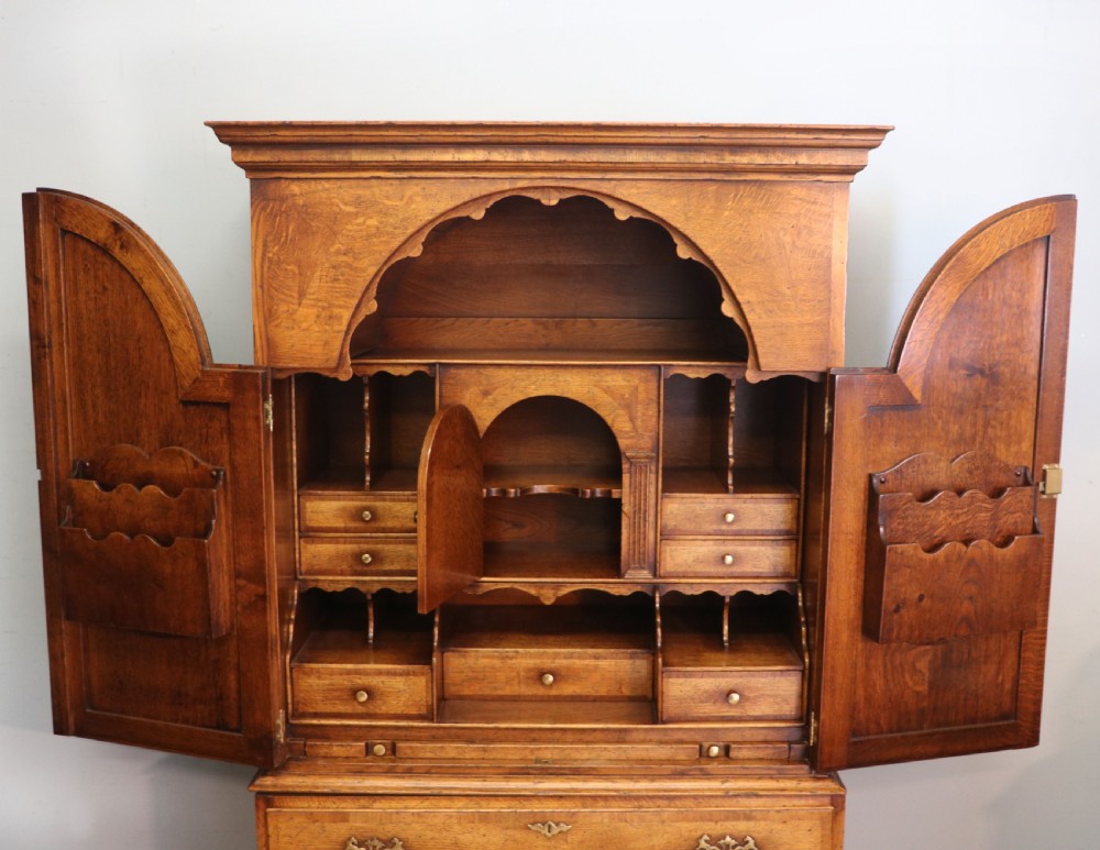 A Georgian style warm brown oak bureau cabinet featuring two upper arched doors opening to a fitted interior of pigeonholes and small drawers above three long drawers with brass handles. View XV