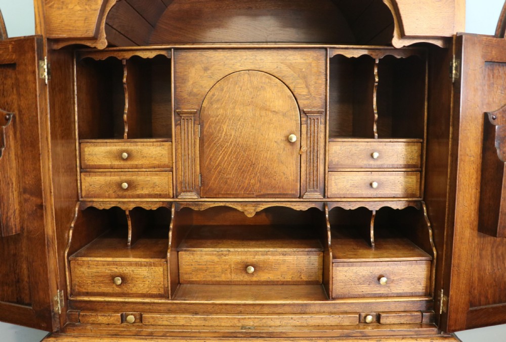 A Georgian style warm brown oak bureau cabinet featuring two upper arched doors opening to a fitted interior of pigeonholes and small drawers above three long drawers with brass handles. View XVI