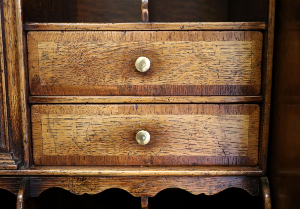 A Georgian style warm brown oak bureau cabinet featuring two upper arched doors opening to a fitted interior of pigeonholes and small drawers above three long drawers with brass handles. View XXI