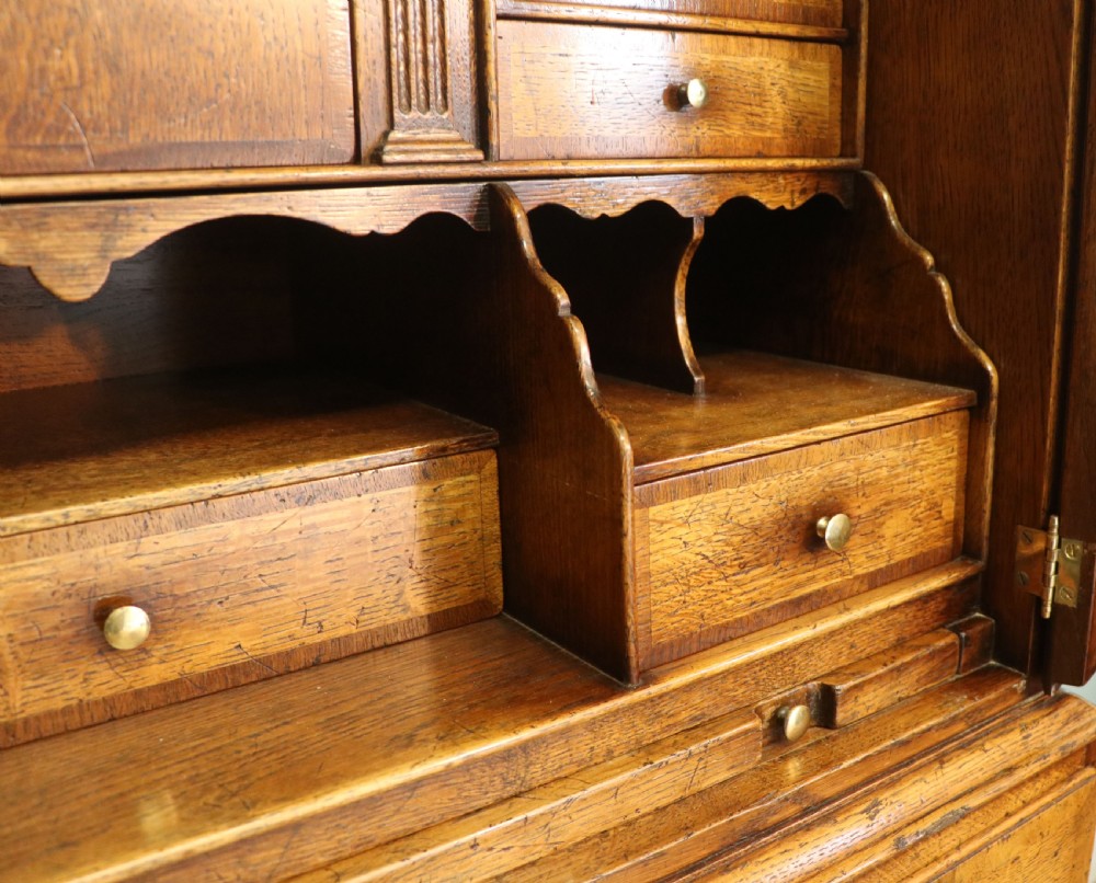 A Georgian style warm brown oak bureau cabinet featuring two upper arched doors opening to a fitted interior of pigeonholes and small drawers above three long drawers with brass handles. View XXV