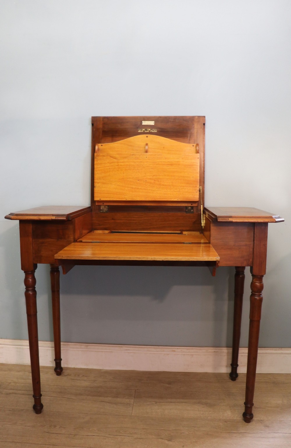 A brown walnut metamorphic writing desk featuring turned legs, side flaps, and an open top section exposing internal stationery compartments. View III