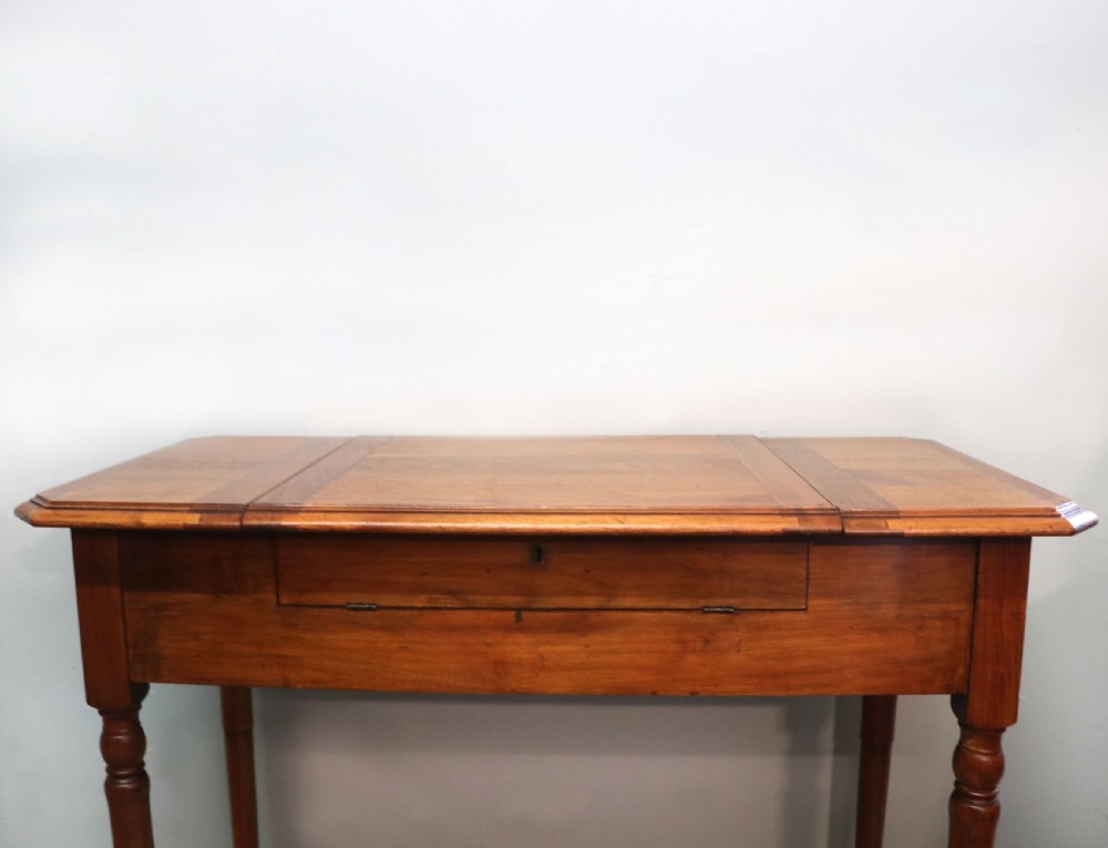 A brown walnut metamorphic writing desk featuring turned legs, side flaps, and an open top section exposing internal stationery compartments. View V