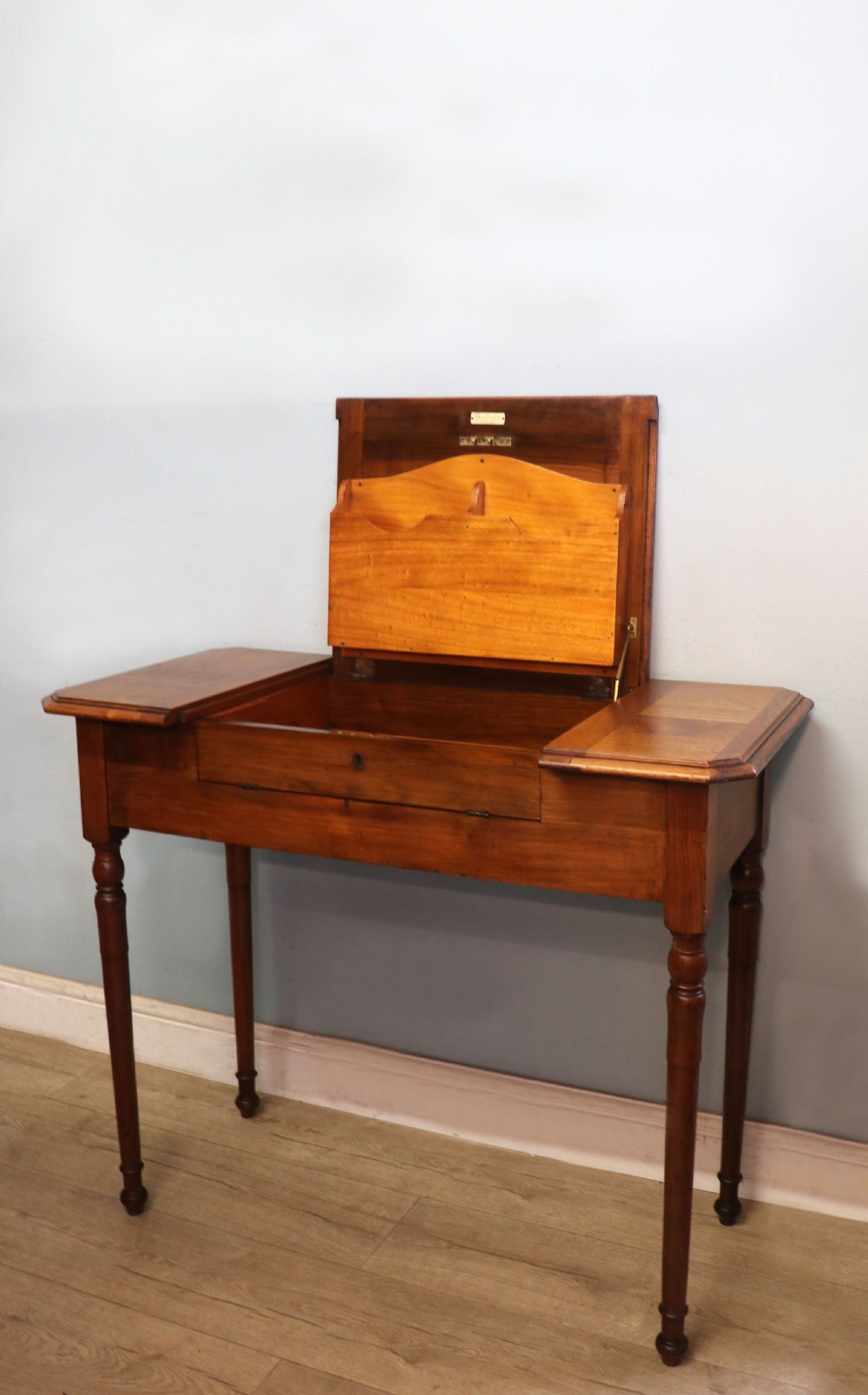 A brown walnut metamorphic writing desk featuring turned legs, side flaps, and an open top section exposing internal stationery compartments. View VI