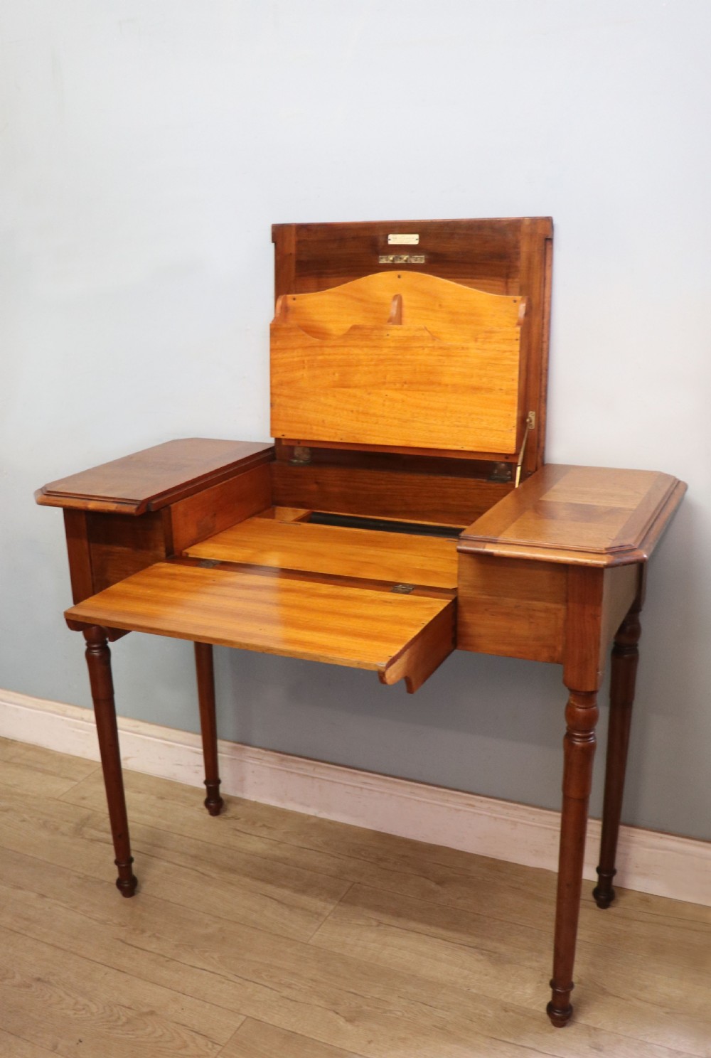 A brown walnut metamorphic writing desk featuring turned legs, side flaps, and an open top section exposing internal stationery compartments. View VII