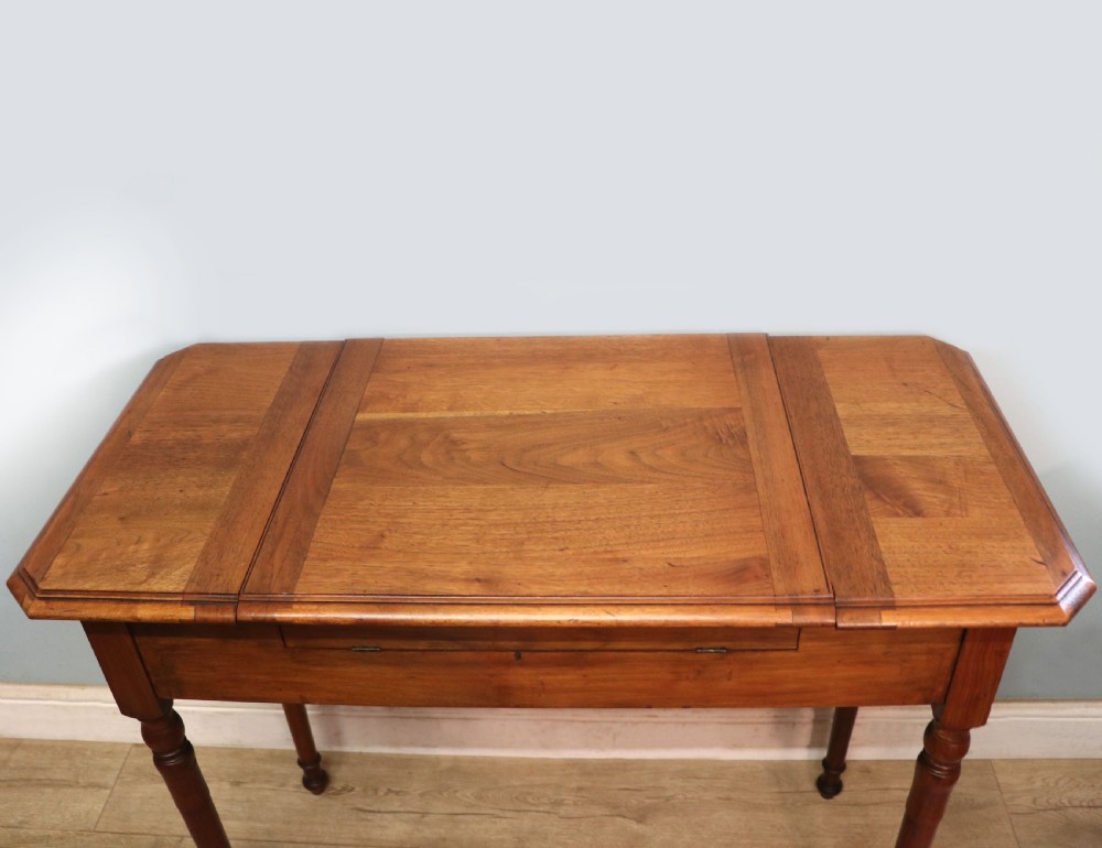 A brown walnut metamorphic writing desk featuring turned legs, side flaps, and an open top section exposing internal stationery compartments. View IX