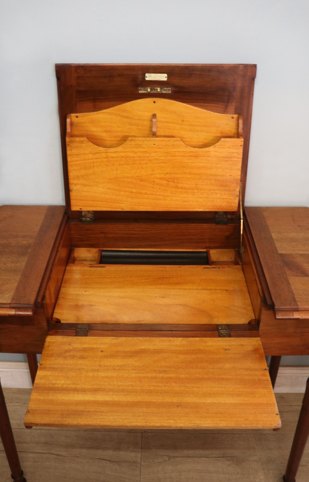A brown walnut metamorphic writing desk featuring turned legs, side flaps, and an open top section exposing internal stationery compartments. View X