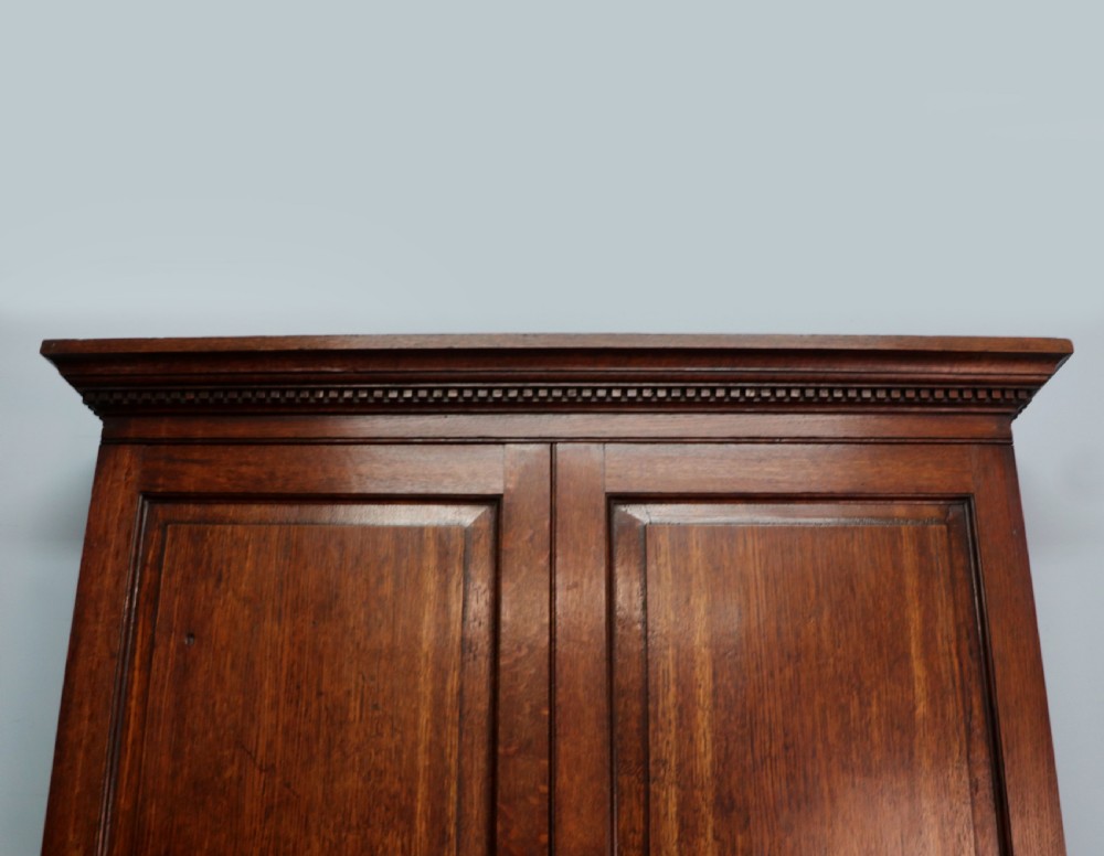 A George III oak bureau bookcase featuring a dentil cornice above two panelled upper doors, a slant-front writing slope opening to a fitted interior, and three long drawers below with brass handles. View XIV