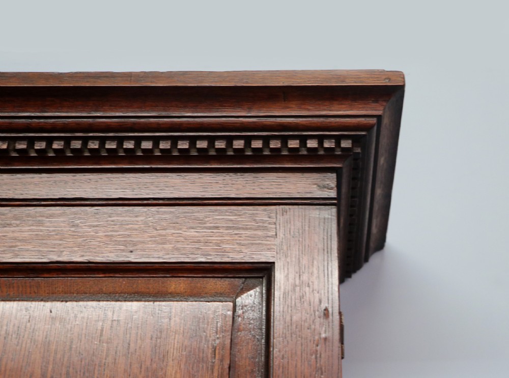 A George III oak bureau bookcase featuring a dentil cornice above two panelled upper doors, a slant-front writing slope opening to a fitted interior, and three long drawers below with brass handles. View XV