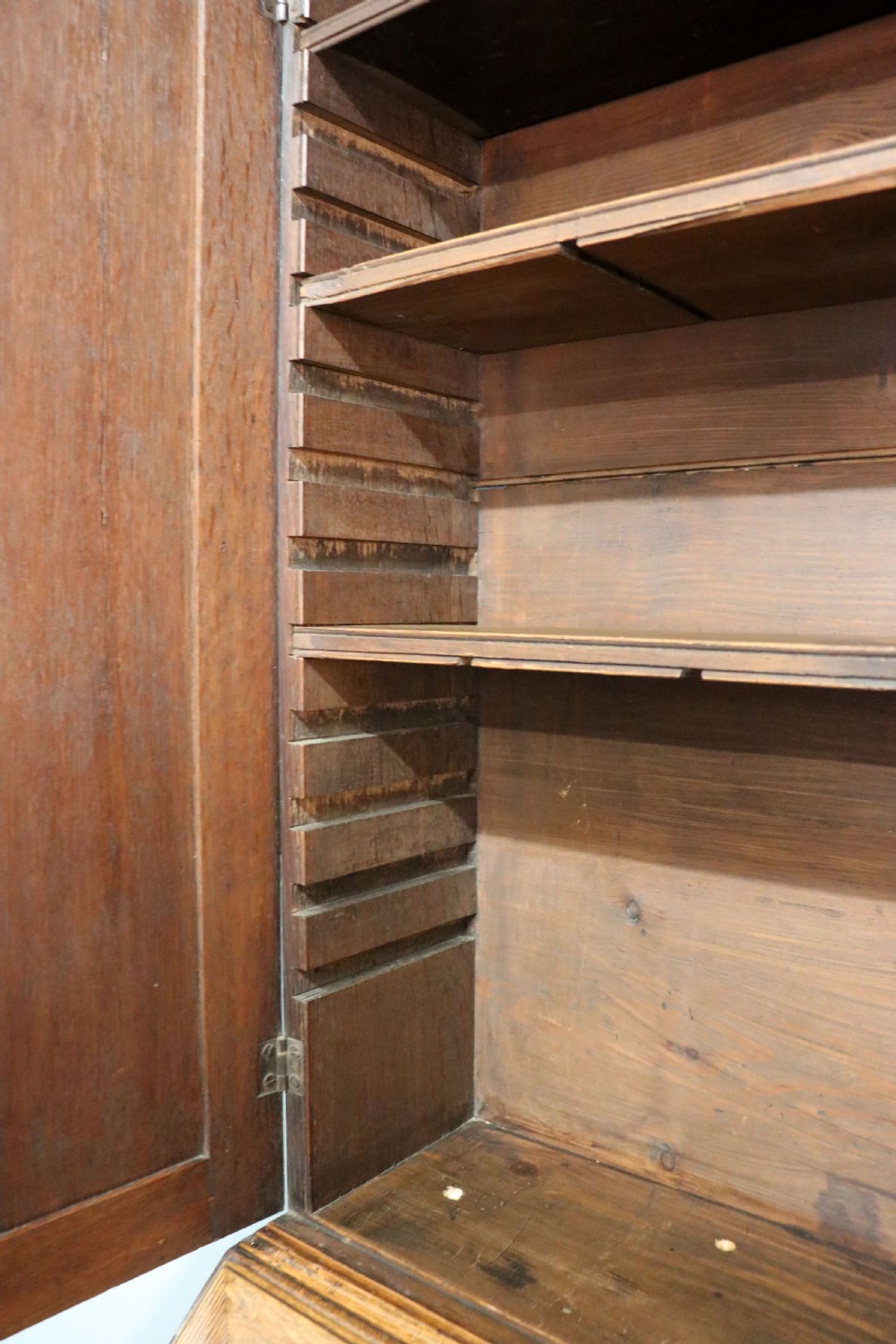 A George III oak bureau bookcase featuring a dentil cornice above two panelled upper doors, a slant-front writing slope opening to a fitted interior, and three long drawers below with brass handles. View XIX