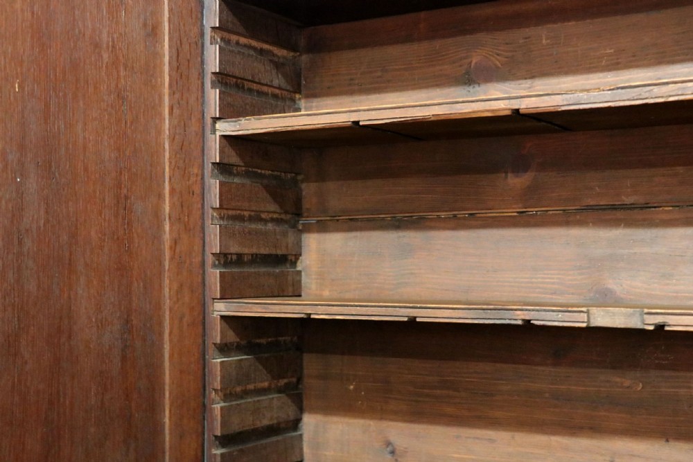 A George III oak bureau bookcase featuring a dentil cornice above two panelled upper doors, a slant-front writing slope opening to a fitted interior, and three long drawers below with brass handles. View XX