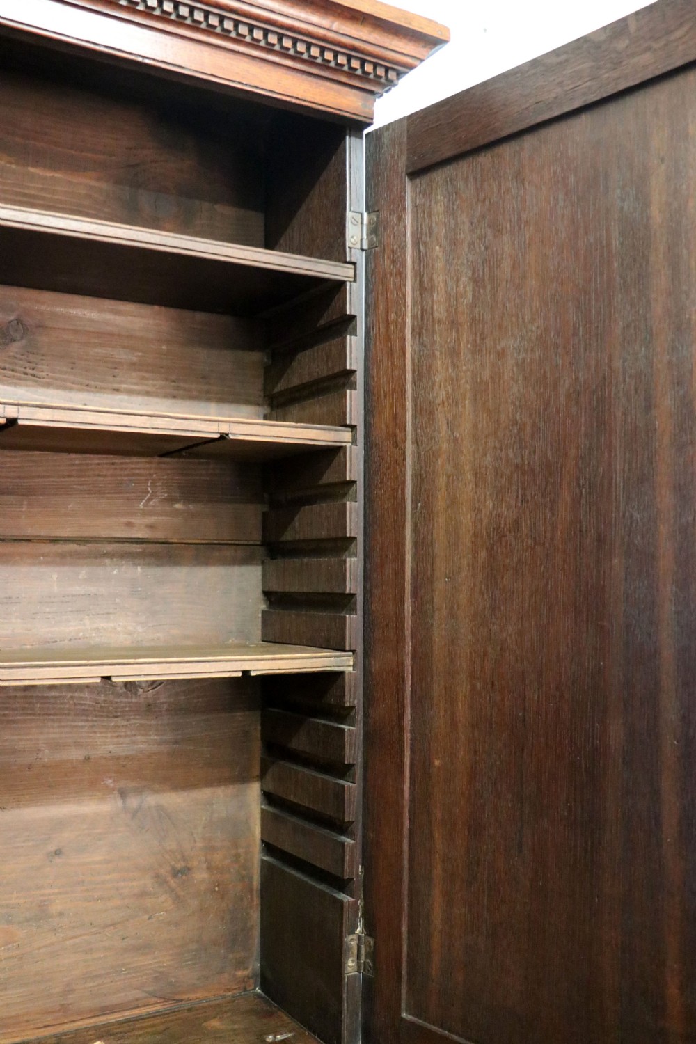 A George III oak bureau bookcase featuring a dentil cornice above two panelled upper doors, a slant-front writing slope opening to a fitted interior, and three long drawers below with brass handles. View XXI
