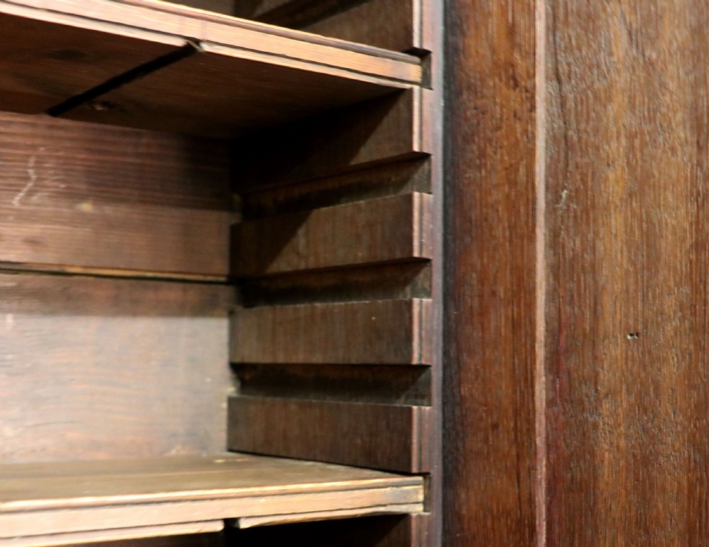 A George III oak bureau bookcase featuring a dentil cornice above two panelled upper doors, a slant-front writing slope opening to a fitted interior, and three long drawers below with brass handles. View XXII