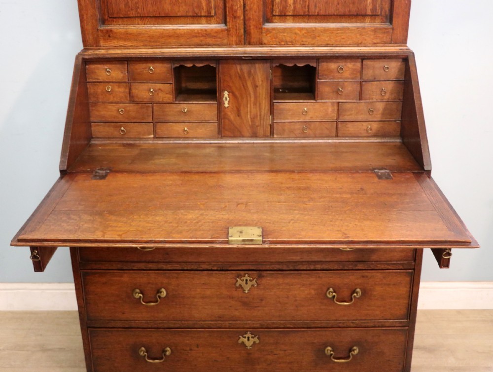A George III oak bureau bookcase featuring a dentil cornice above two panelled upper doors, a slant-front writing slope opening to a fitted interior, and three long drawers below with brass handles. View XXVI