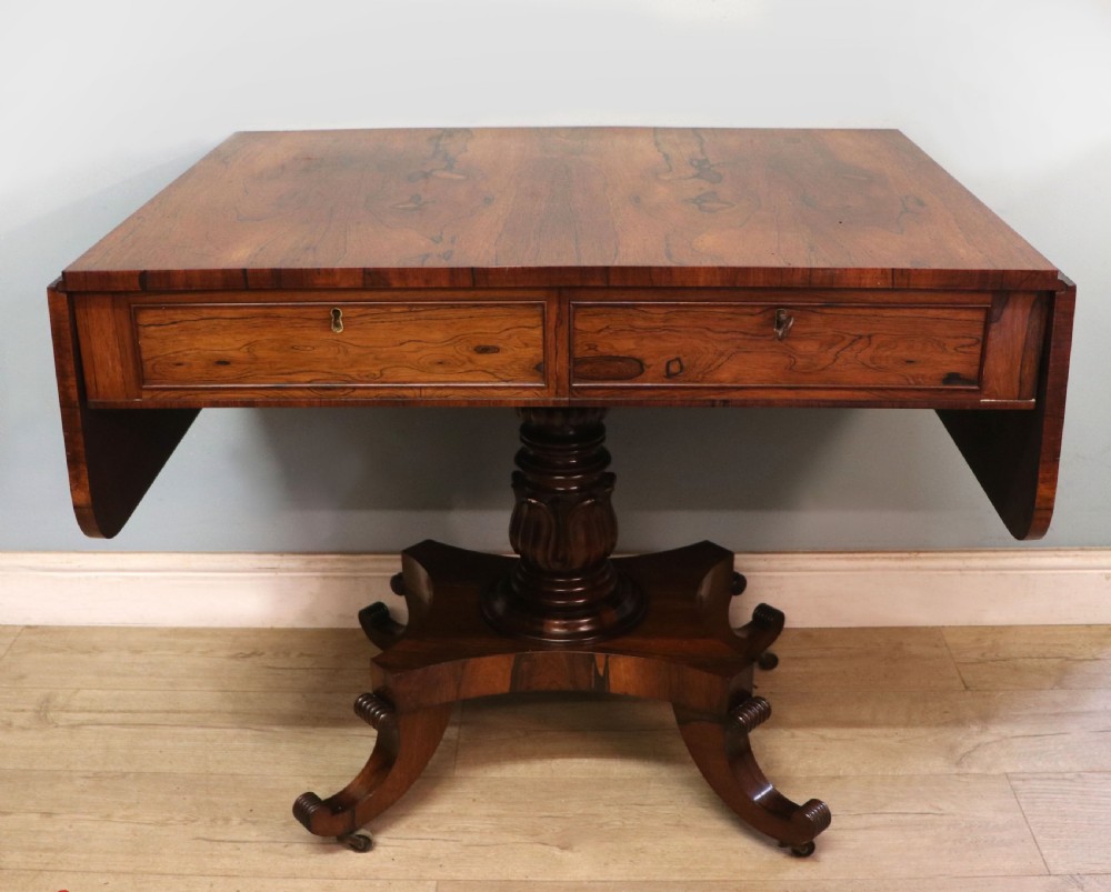 A late Georgian drop-leaf sofa table crafted from dark figured rosewood with a turned pedestal stem, two frieze drawers, and splayed quadruped legs with brass castors. View II