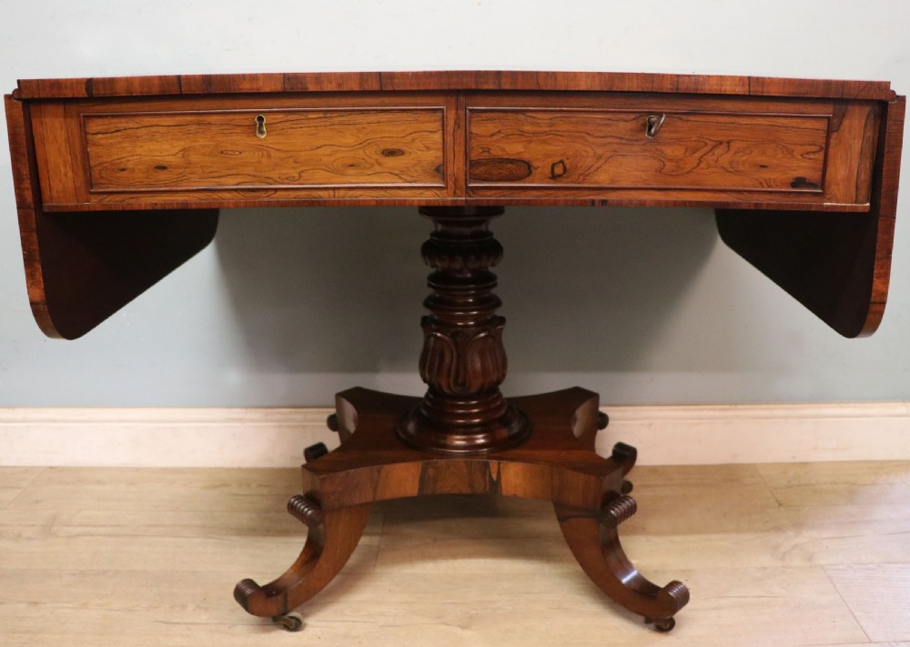 A late Georgian drop-leaf sofa table crafted from dark figured rosewood with a turned pedestal stem, two frieze drawers, and splayed quadruped legs with brass castors. View III