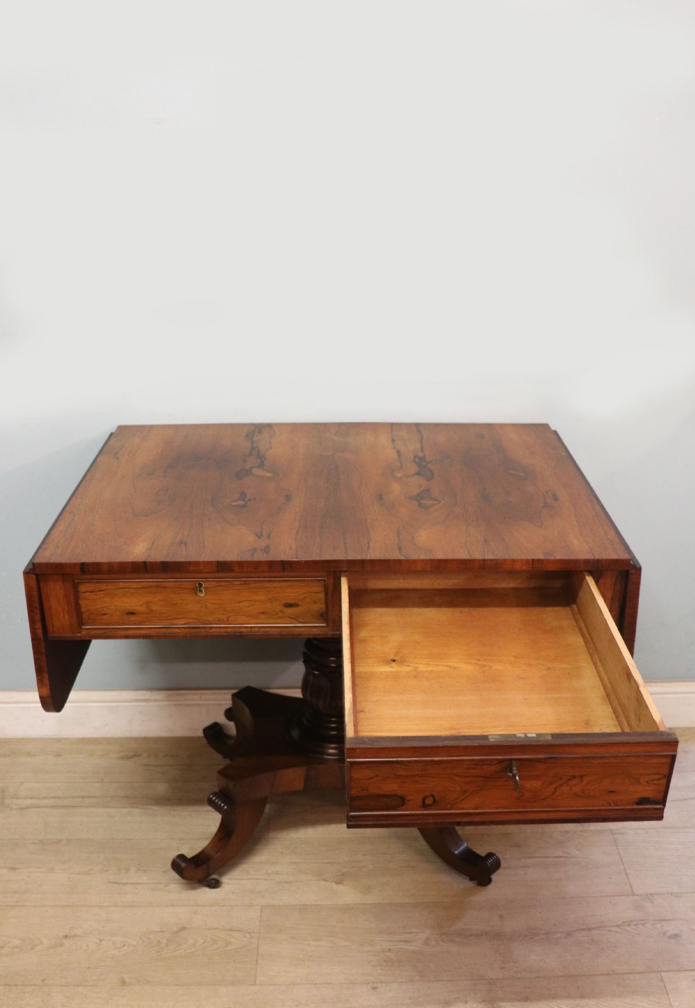 A late Georgian drop-leaf sofa table crafted from dark figured rosewood with a turned pedestal stem, two frieze drawers, and splayed quadruped legs with brass castors. View IV