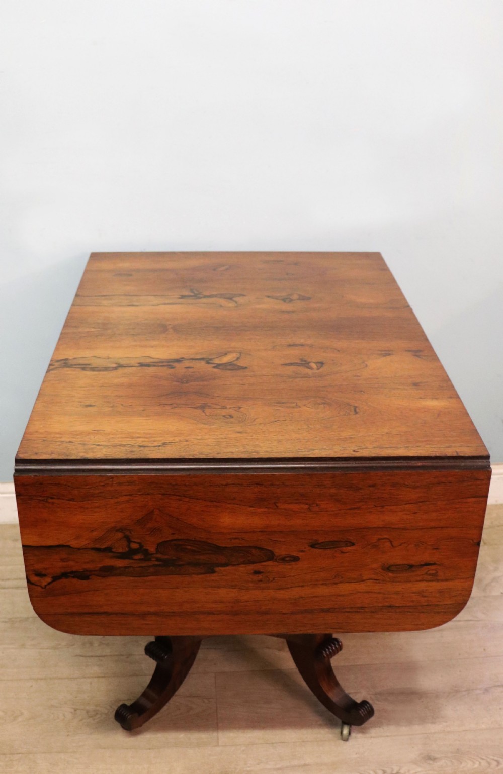 A late Georgian drop-leaf sofa table crafted from dark figured rosewood with a turned pedestal stem, two frieze drawers, and splayed quadruped legs with brass castors. View VI