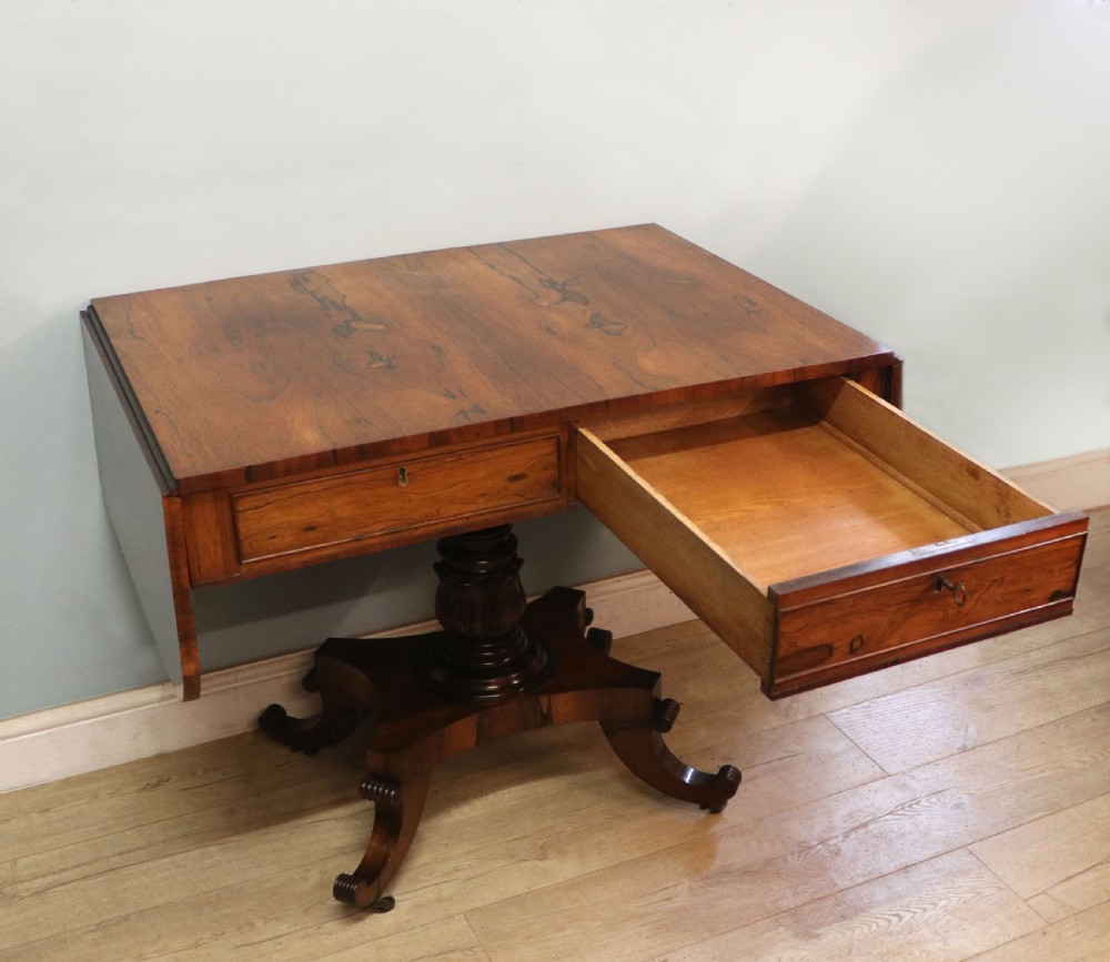 A late Georgian drop-leaf sofa table crafted from dark figured rosewood with a turned pedestal stem, two frieze drawers, and splayed quadruped legs with brass castors. View VII