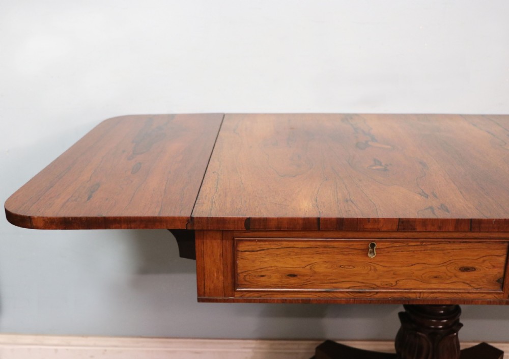 A late Georgian drop-leaf sofa table crafted from dark figured rosewood with a turned pedestal stem, two frieze drawers, and splayed quadruped legs with brass castors. View VIII