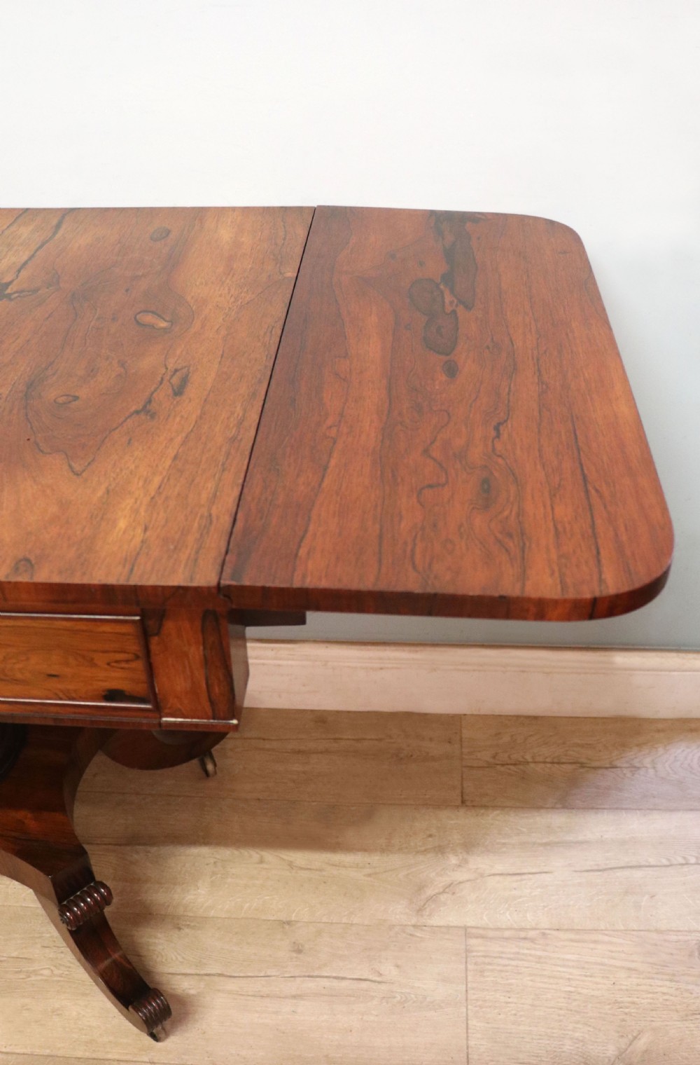 A late Georgian drop-leaf sofa table crafted from dark figured rosewood with a turned pedestal stem, two frieze drawers, and splayed quadruped legs with brass castors. View IX