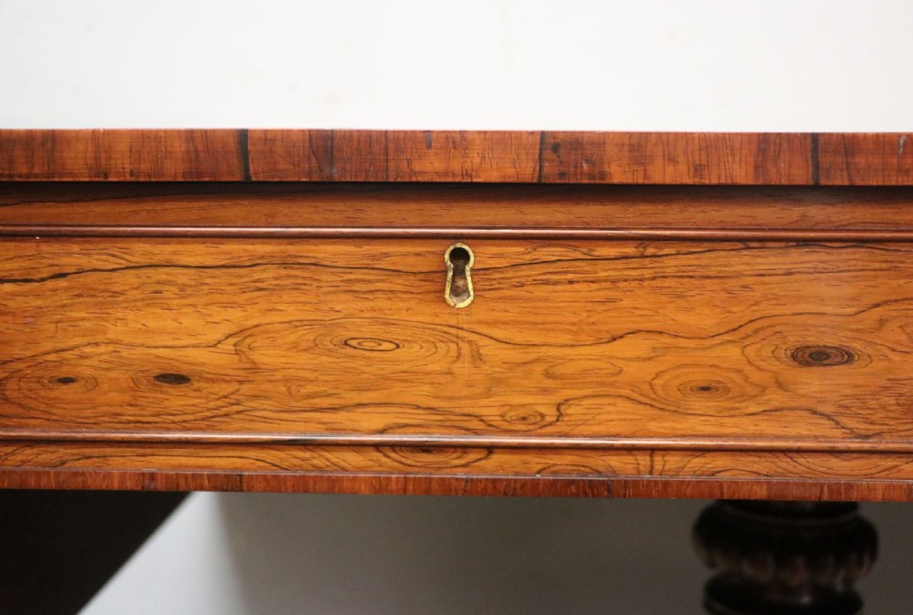 A late Georgian drop-leaf sofa table crafted from dark figured rosewood with a turned pedestal stem, two frieze drawers, and splayed quadruped legs with brass castors. View XII