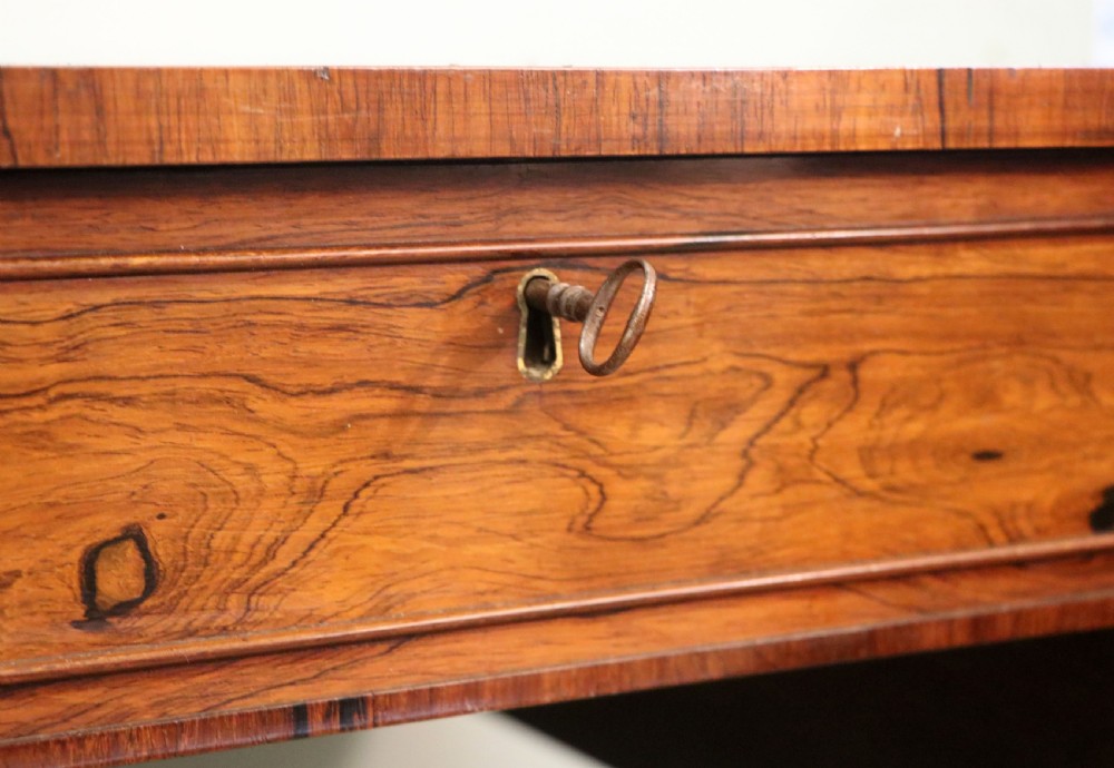 A late Georgian drop-leaf sofa table crafted from dark figured rosewood with a turned pedestal stem, two frieze drawers, and splayed quadruped legs with brass castors. View XIII