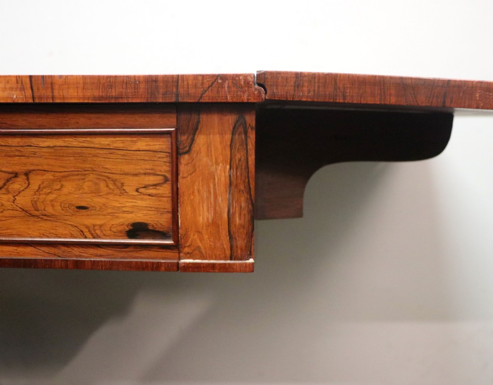 A late Georgian drop-leaf sofa table crafted from dark figured rosewood with a turned pedestal stem, two frieze drawers, and splayed quadruped legs with brass castors. View XIV