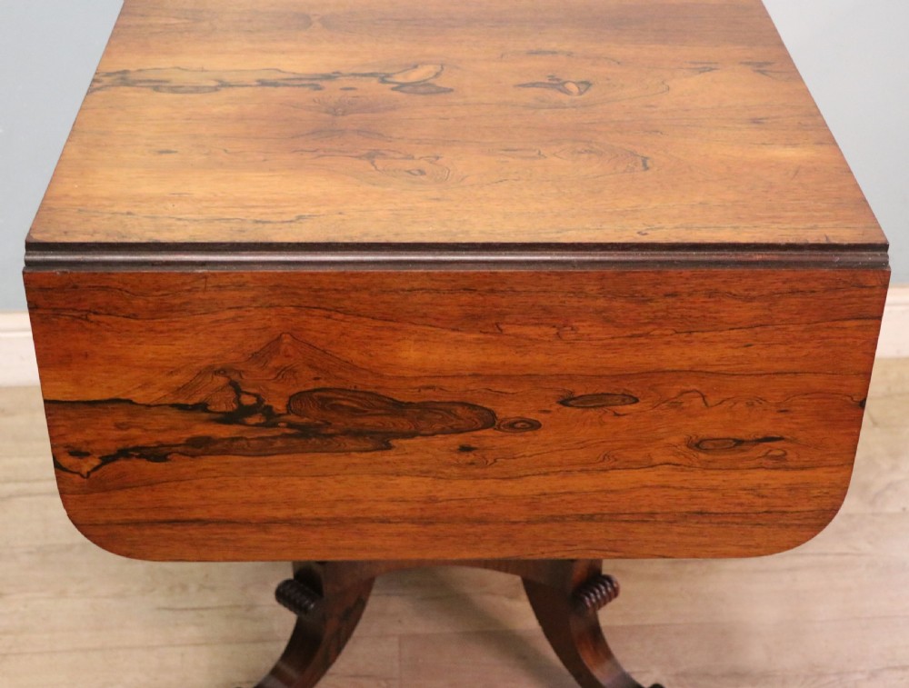 A late Georgian drop-leaf sofa table crafted from dark figured rosewood with a turned pedestal stem, two frieze drawers, and splayed quadruped legs with brass castors. View XVIII