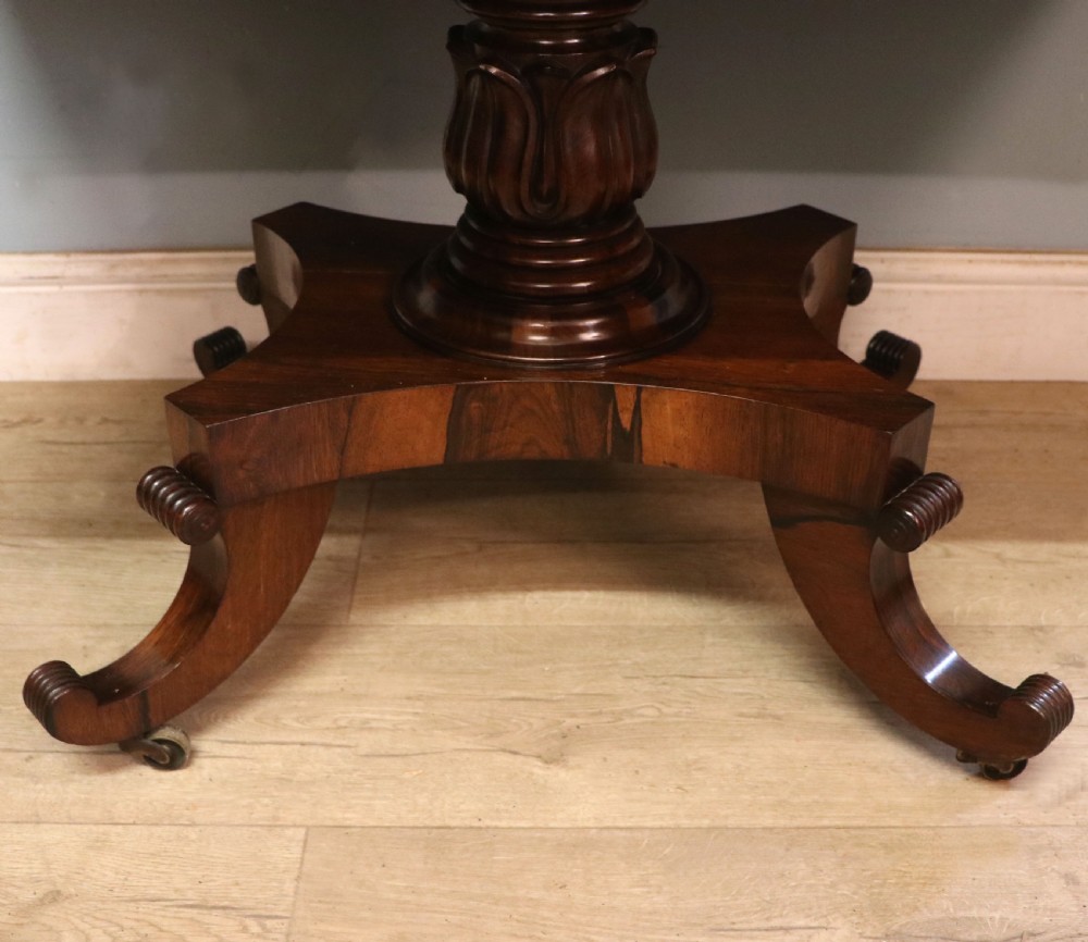 A late Georgian drop-leaf sofa table crafted from dark figured rosewood with a turned pedestal stem, two frieze drawers, and splayed quadruped legs with brass castors. View XXV