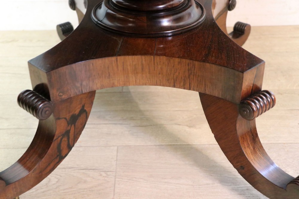 A late Georgian drop-leaf sofa table crafted from dark figured rosewood with a turned pedestal stem, two frieze drawers, and splayed quadruped legs with brass castors. View XXVIII