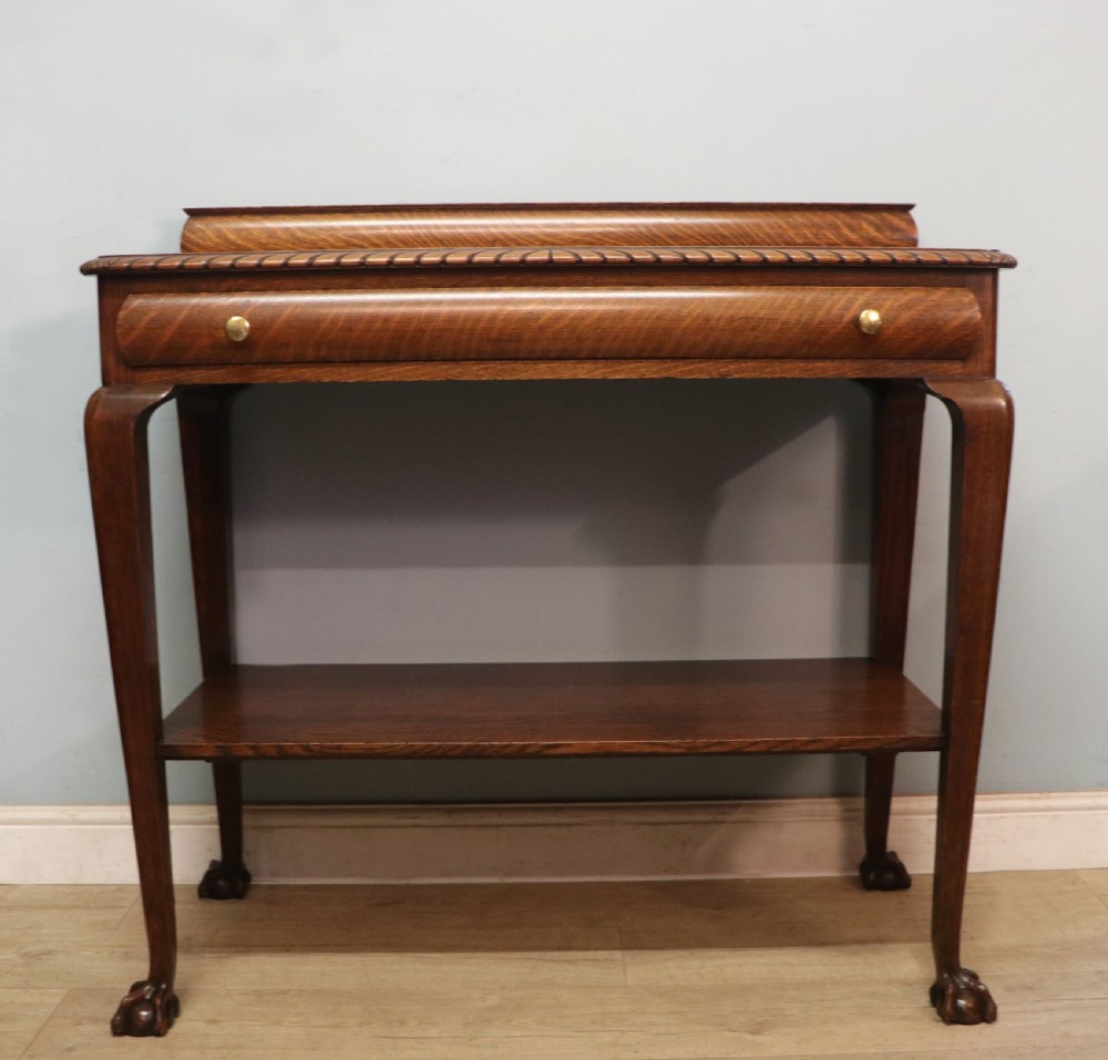 A Georgian revival oak side table featuring a single drawer with brass knobs, a lower tier shelf, and cabriole legs terminating in carved claw and ball feet.