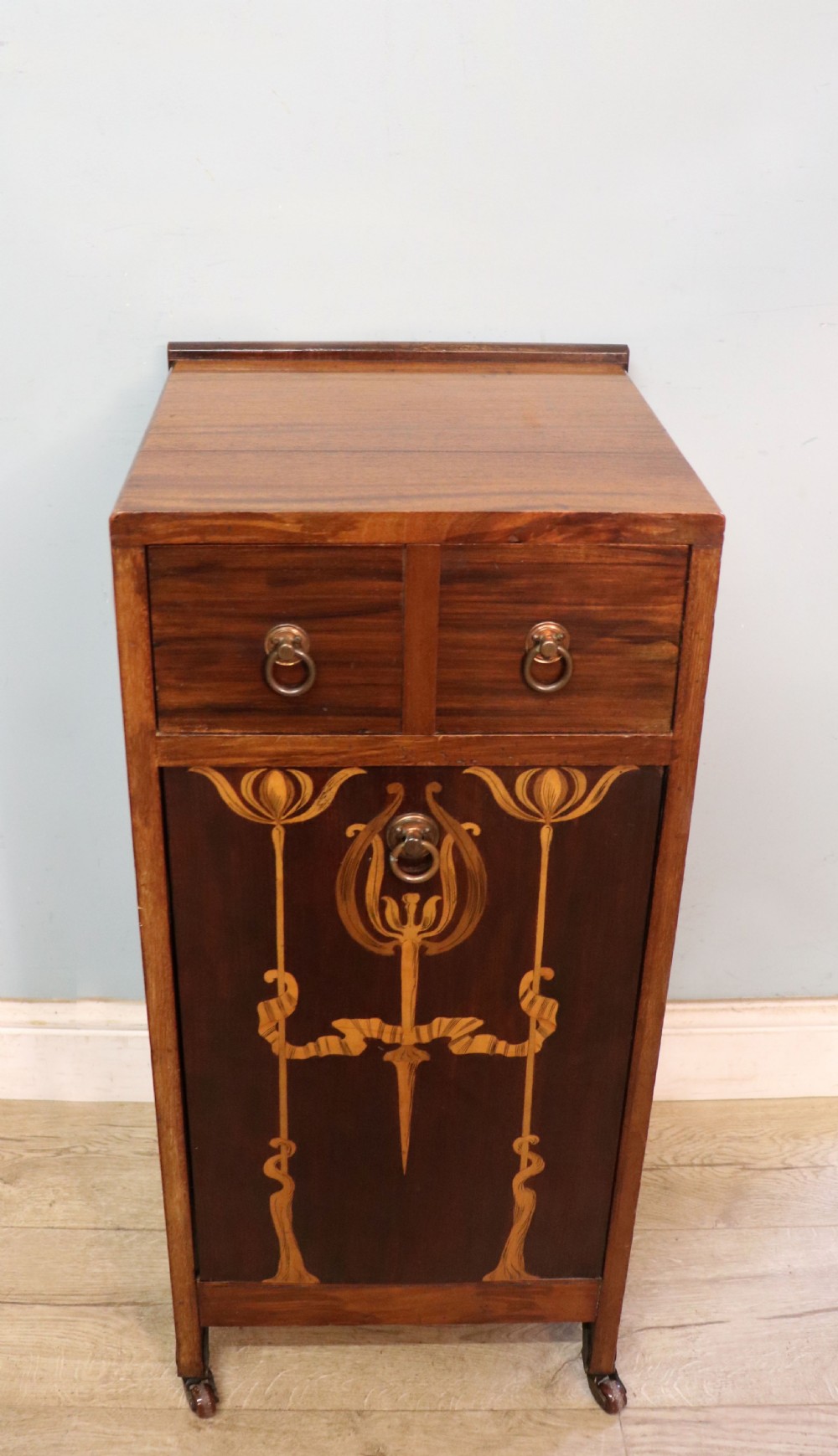 A tall dark wood Art Nouveau coal box featuring botanical marquetry inlay and brass ring handles, supported on castors. View VI