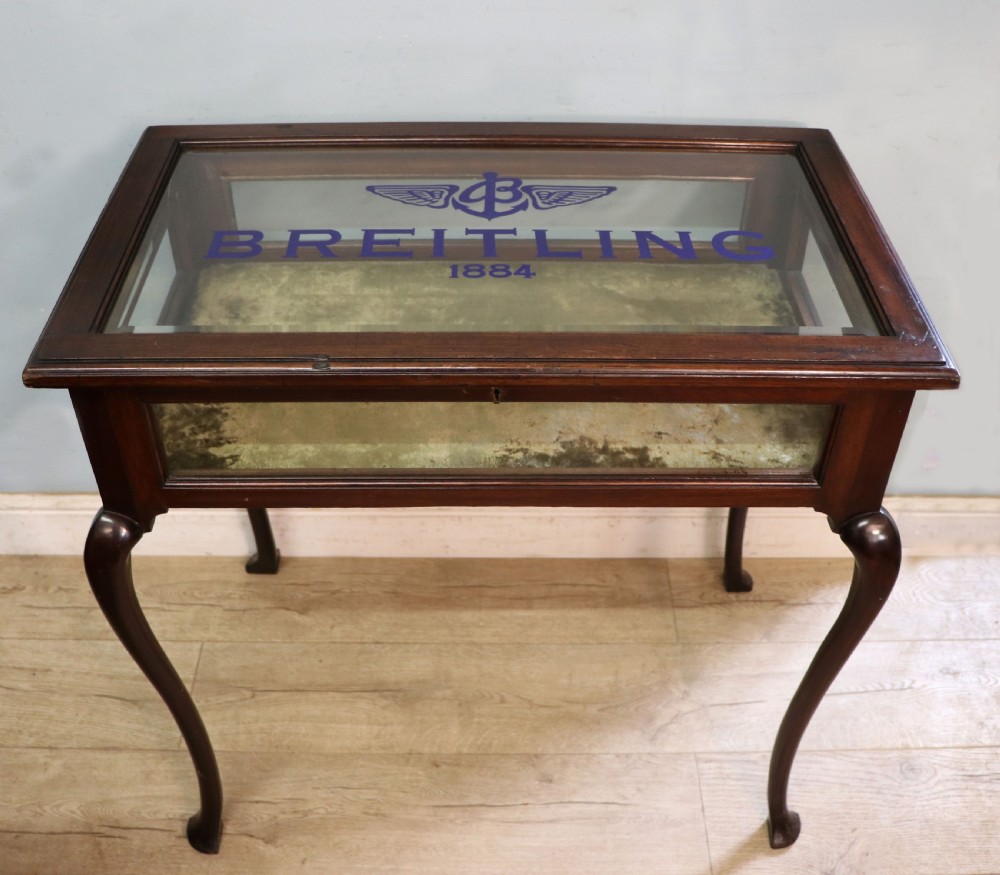 A dark mahogany glazed bijouterie table featuring cabriole legs, a glass top with blue Breitling watch branding, and a lined interior display compartment.