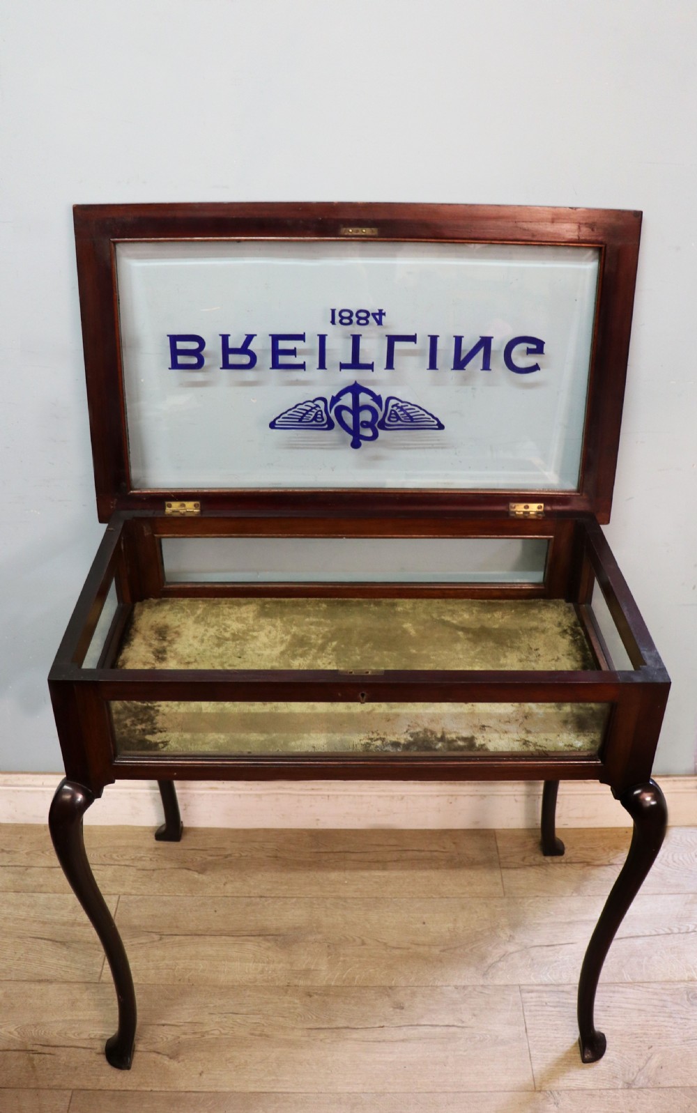 A dark mahogany glazed bijouterie table featuring cabriole legs, a glass top with blue Breitling watch branding, and a lined interior display compartment. View III