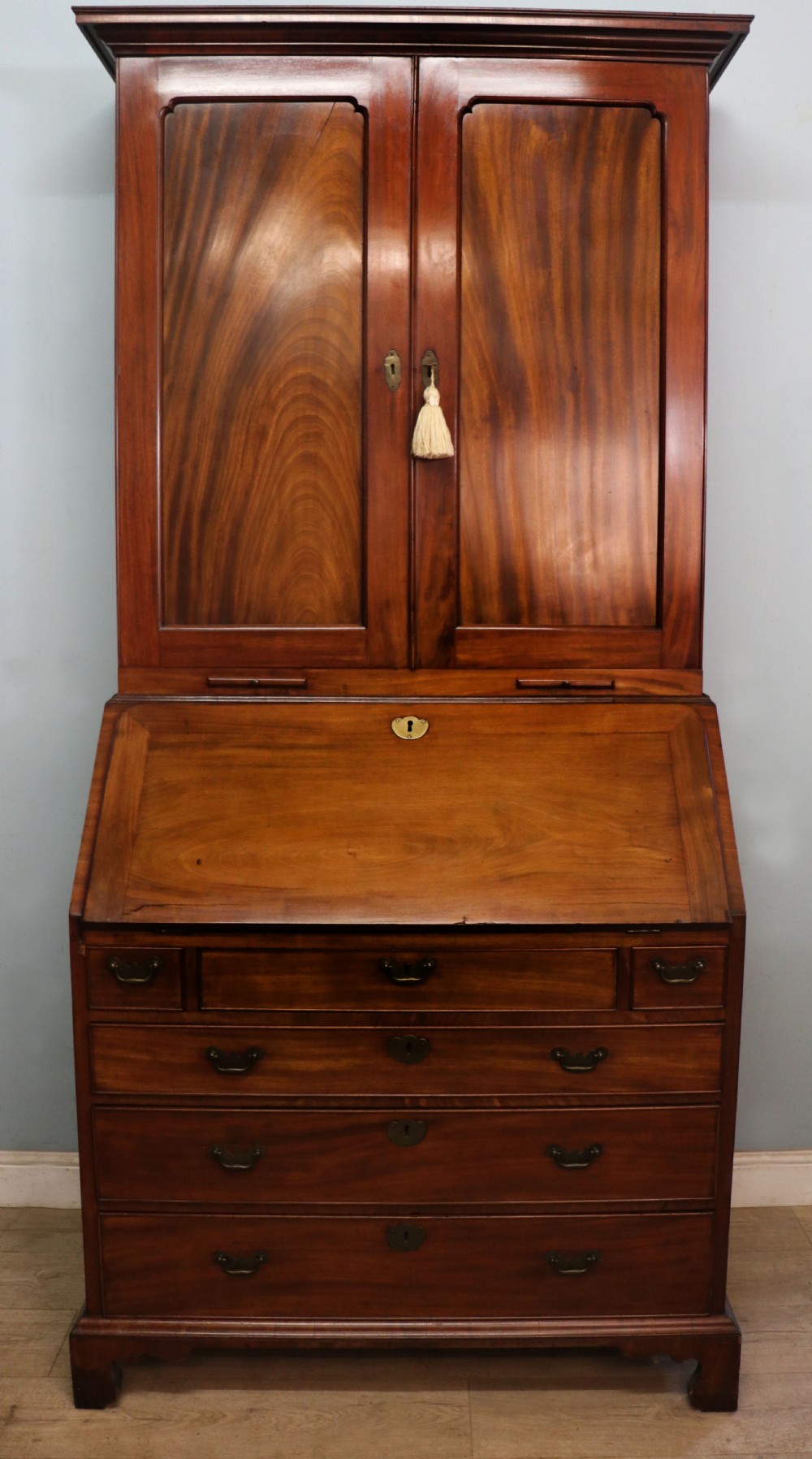 A George III mahogany bureau bookcase featuring a panelled upper cabinet above a fall-front writing surface and graduated drawers with brass hardware. View II