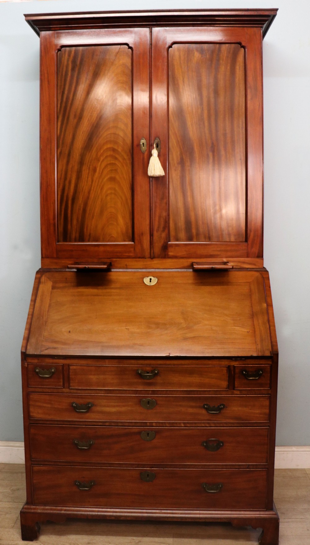 A George III mahogany bureau bookcase featuring a panelled upper cabinet above a fall-front writing surface and graduated drawers with brass hardware.