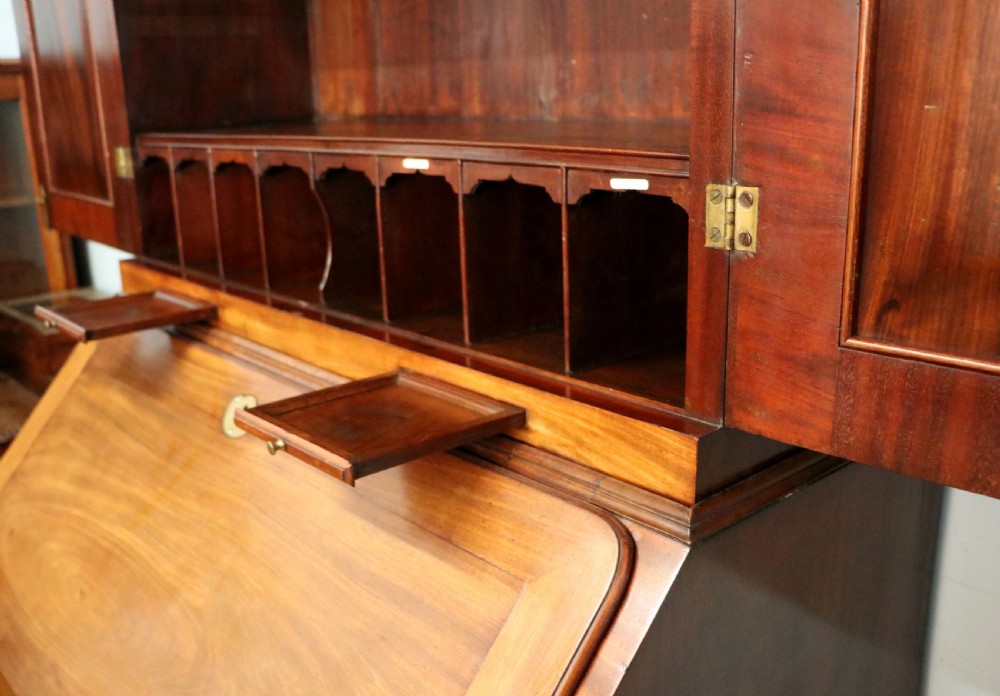 A George III mahogany bureau bookcase featuring a panelled upper cabinet above a fall-front writing surface and graduated drawers with brass hardware. View XXVI