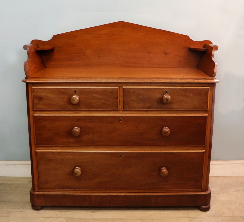A mid-nineteenth century mahogany chest of drawers featuring two short drawers over two long drawers, turned wooden handles, and a shaped galleried backboard.