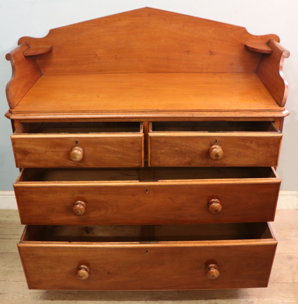 A mid-nineteenth century mahogany chest of drawers featuring two short drawers over two long drawers, turned wooden handles, and a shaped galleried backboard. View IV