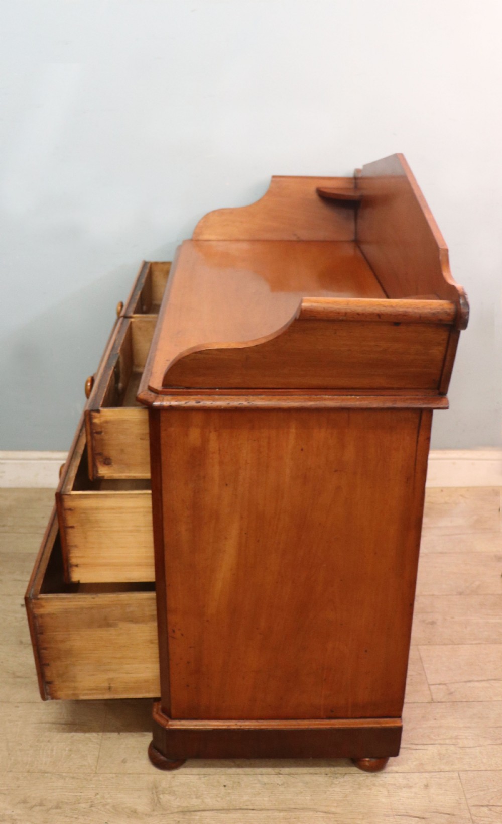 A mid-nineteenth century mahogany chest of drawers featuring two short drawers over two long drawers, turned wooden handles, and a shaped galleried backboard. View VI