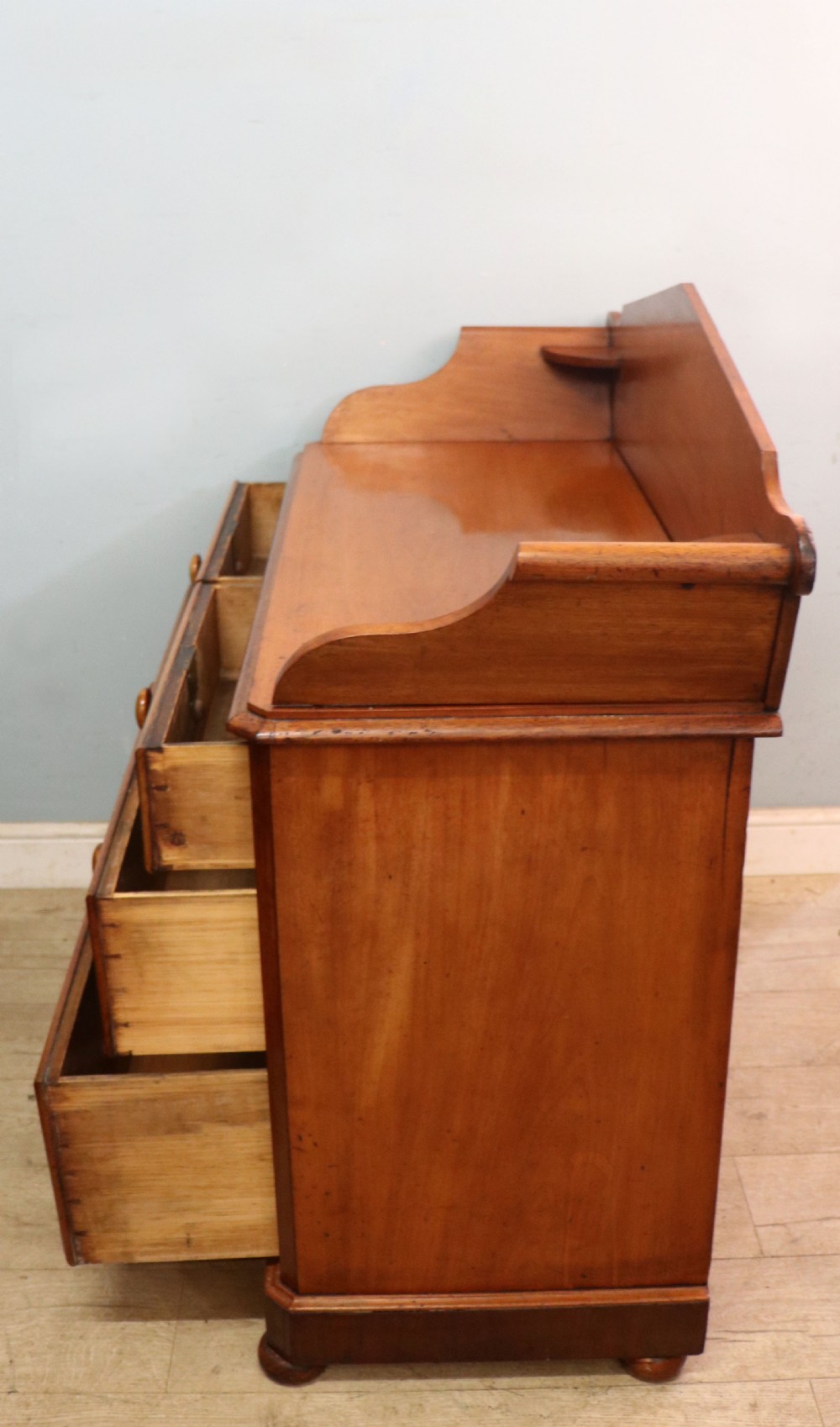 A mid-nineteenth century mahogany chest of drawers featuring two short drawers over two long drawers, turned wooden handles, and a shaped galleried backboard. View XVII