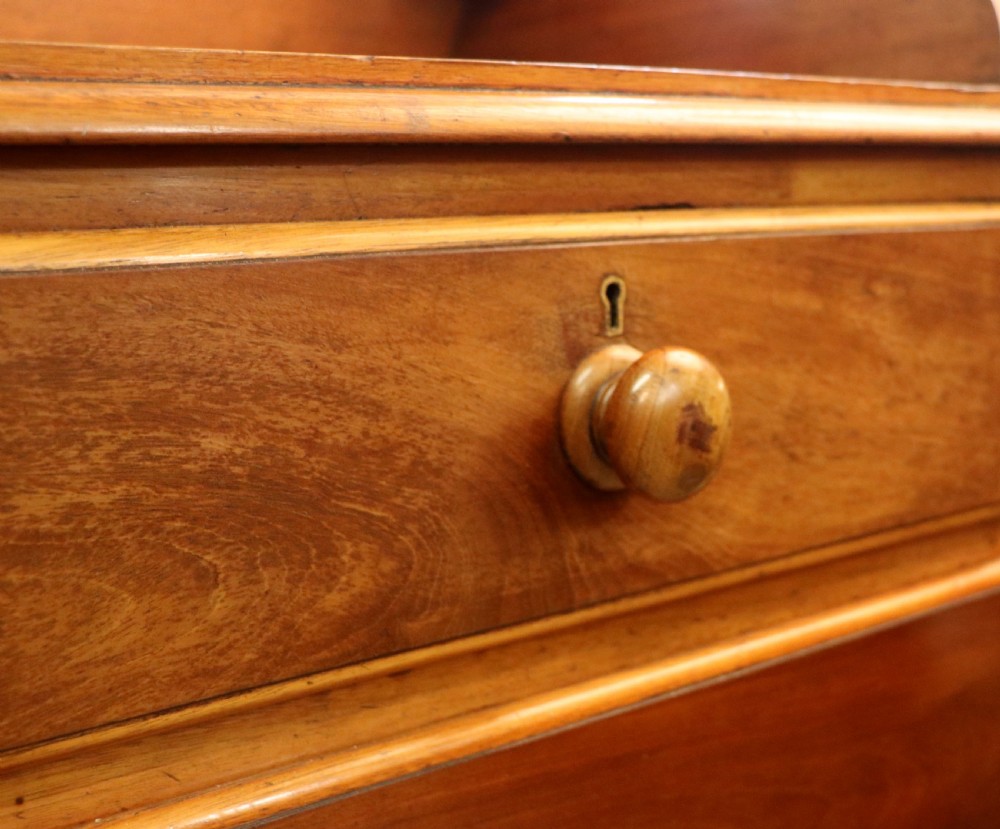 A mid-nineteenth century mahogany chest of drawers featuring two short drawers over two long drawers, turned wooden handles, and a shaped galleried backboard. View XVIII