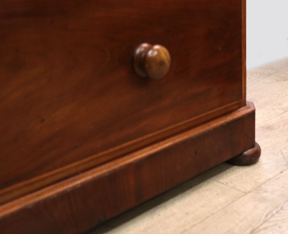 A mid-nineteenth century mahogany chest of drawers featuring two short drawers over two long drawers, turned wooden handles, and a shaped galleried backboard. View XXIV