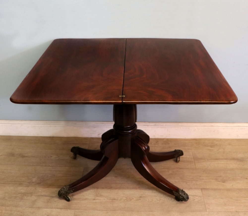 An early 19th-century mahogany tea table featuring a hinged fold-over top, turned central column, and four splayed legs with brass castors.