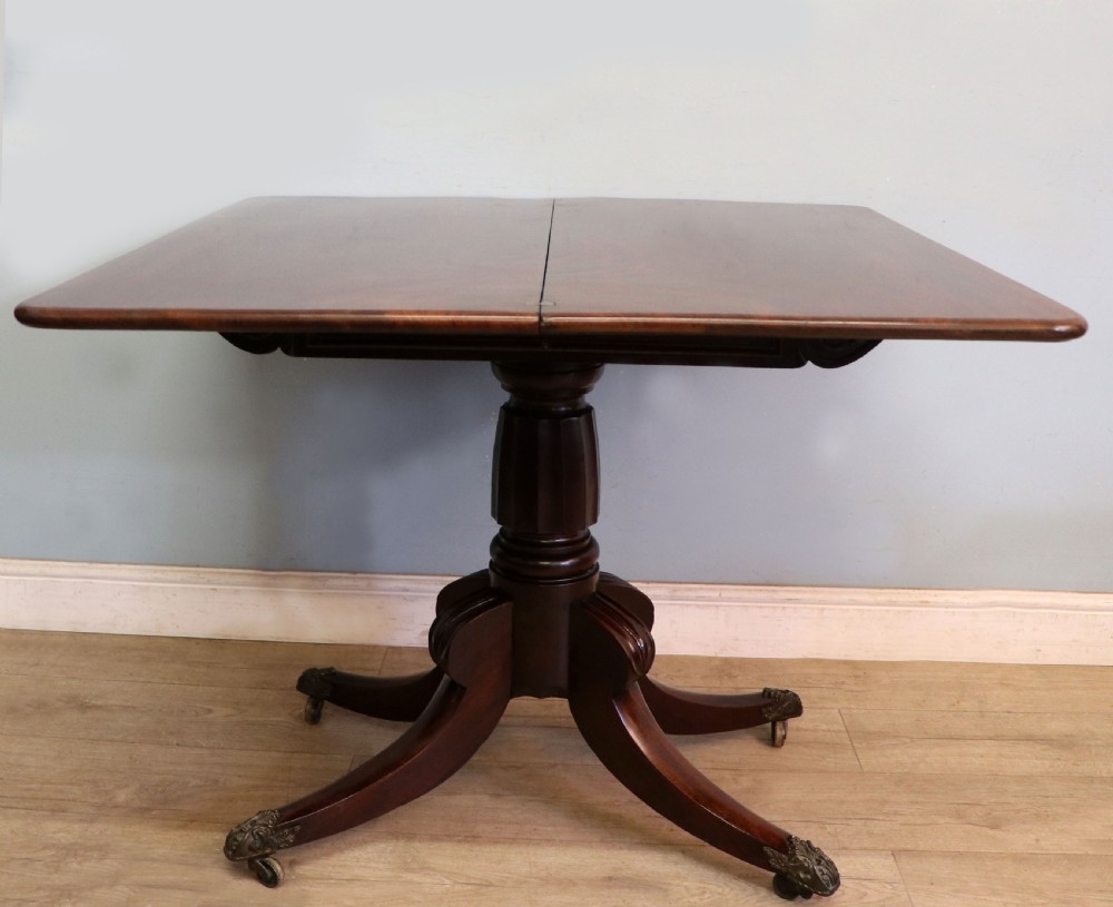 An early 19th-century mahogany tea table featuring a hinged fold-over top, turned central column, and four splayed legs with brass castors. View II